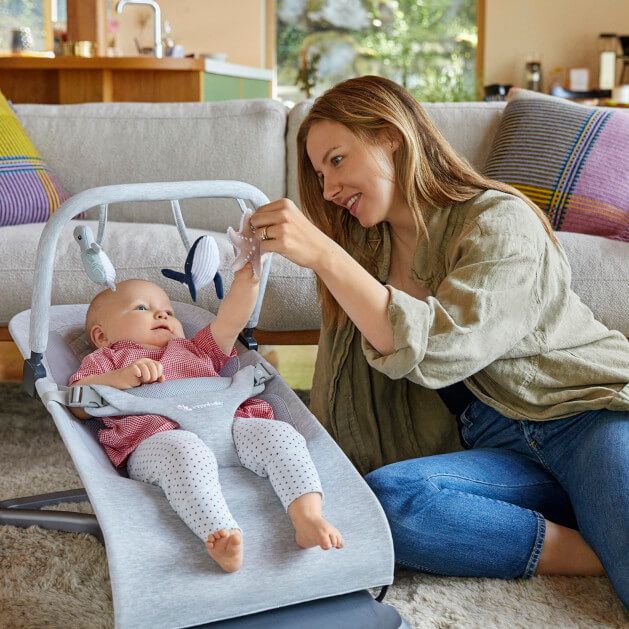 mother playing with child sitting on a bouncy chair